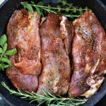 Top view of marinated beef steaks seasoned with herbs and spices in a non-stick pan.